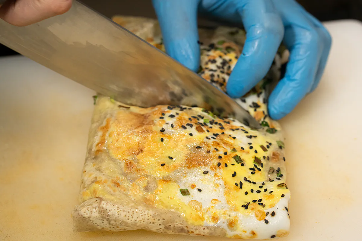 Cutting a Chinese egg pancake with sesame seeds and scallions at Me + Crêpe, a Chinese Restaurant in Pasadena
